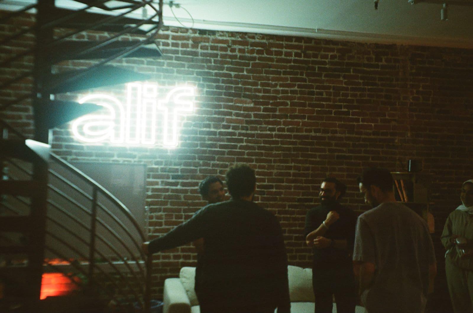 Founders talking under the neon Alif sign at an evening in San Francisco